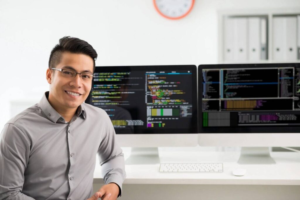 Man smiling in front of computer screens.